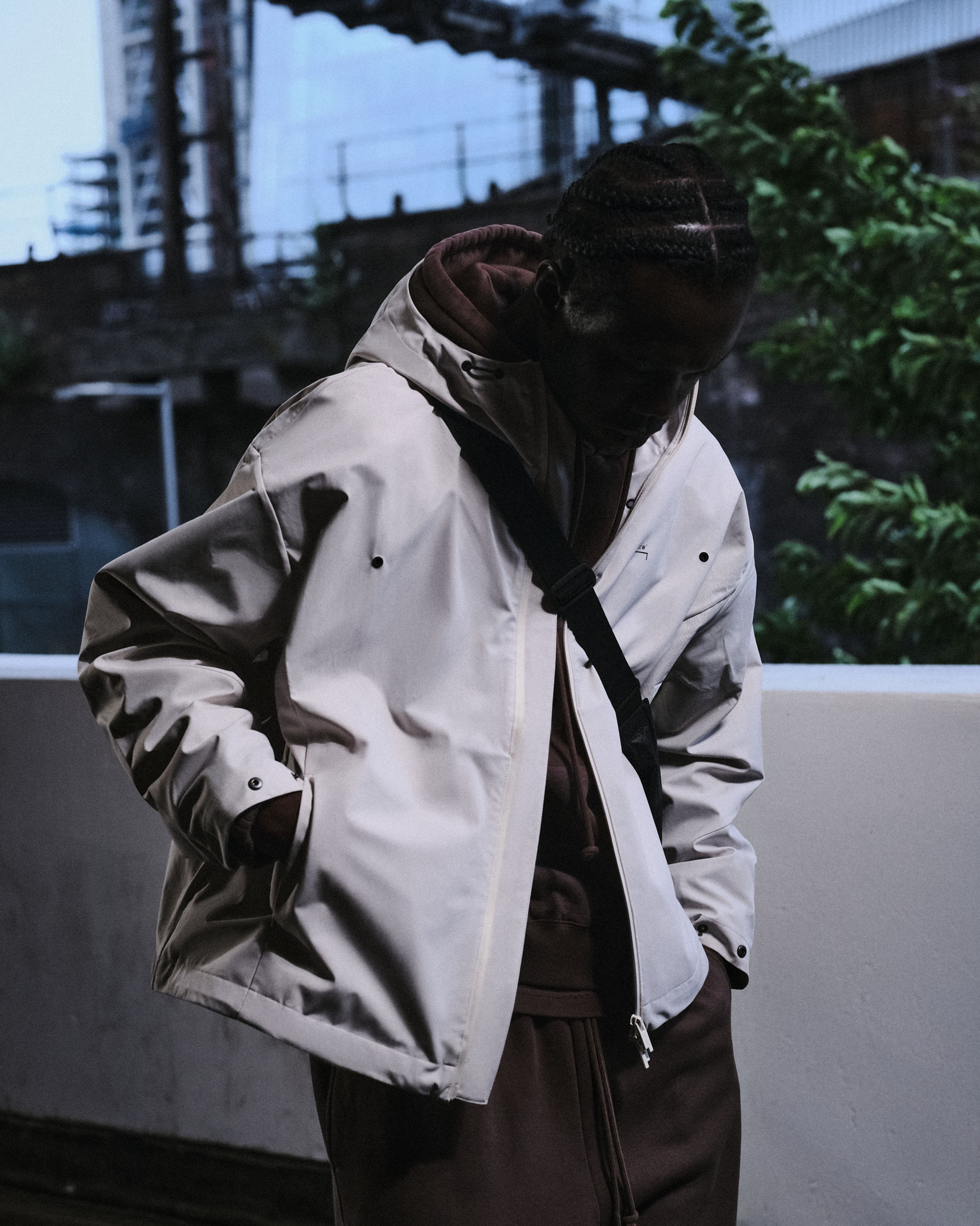 Man wearing a white hooded jacket over a brown hoodie with an urban industrial background