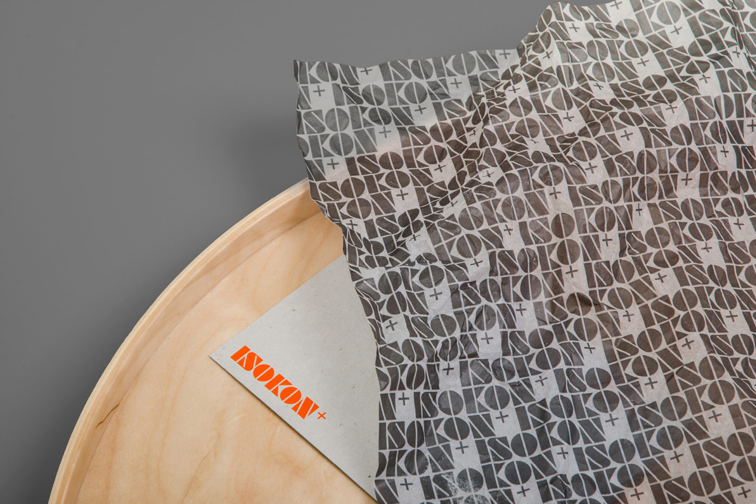 Printed tissue paper featuring repeating ISOKON+ branding resting on a light wood tray against a grey background