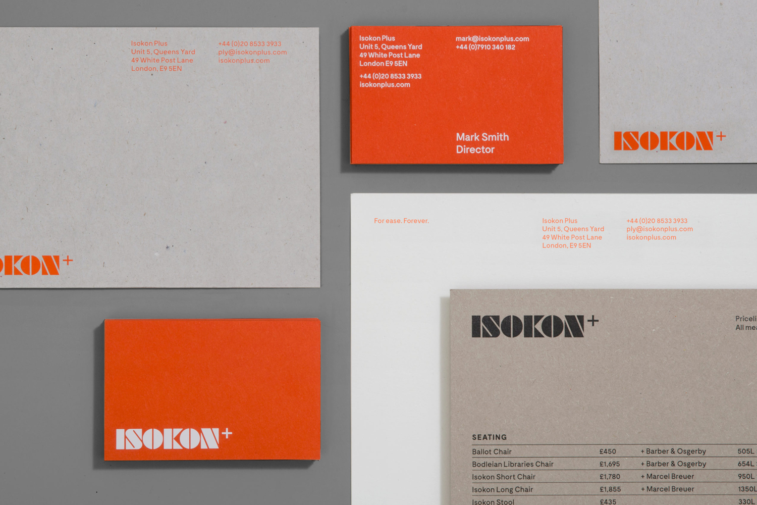 Stationery suite for Isokon Furniture Company featuring orange business cards, grey letterhead, and branded envelopes on a grey surface.