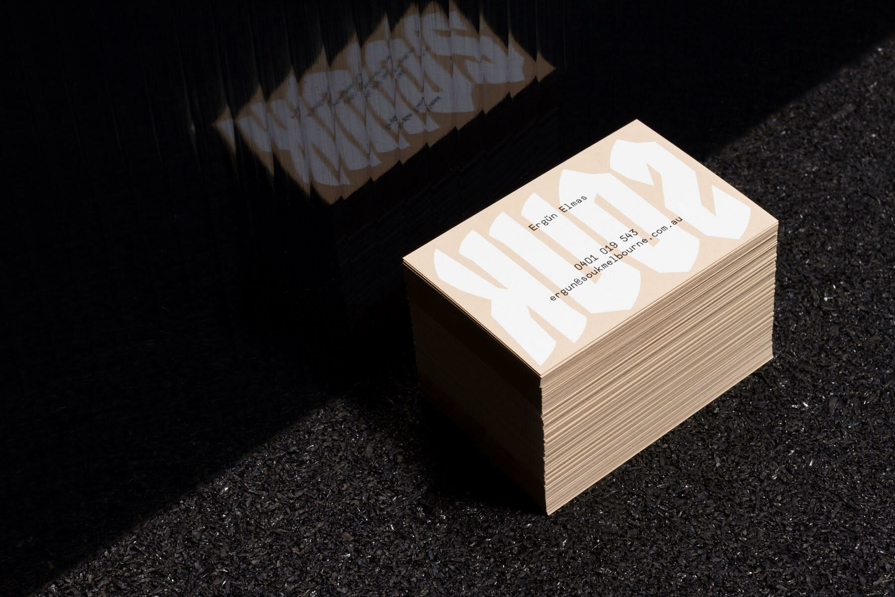 A stack of cream-colored business cards with bold typography on a dark surface reflecting the brand name