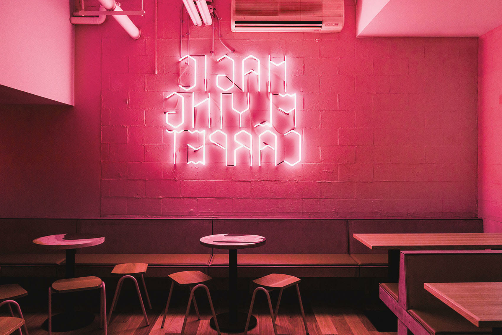 Interior cafe view featuring a glowing pink neon sign on a textured brick wall above built-in seating and small tables