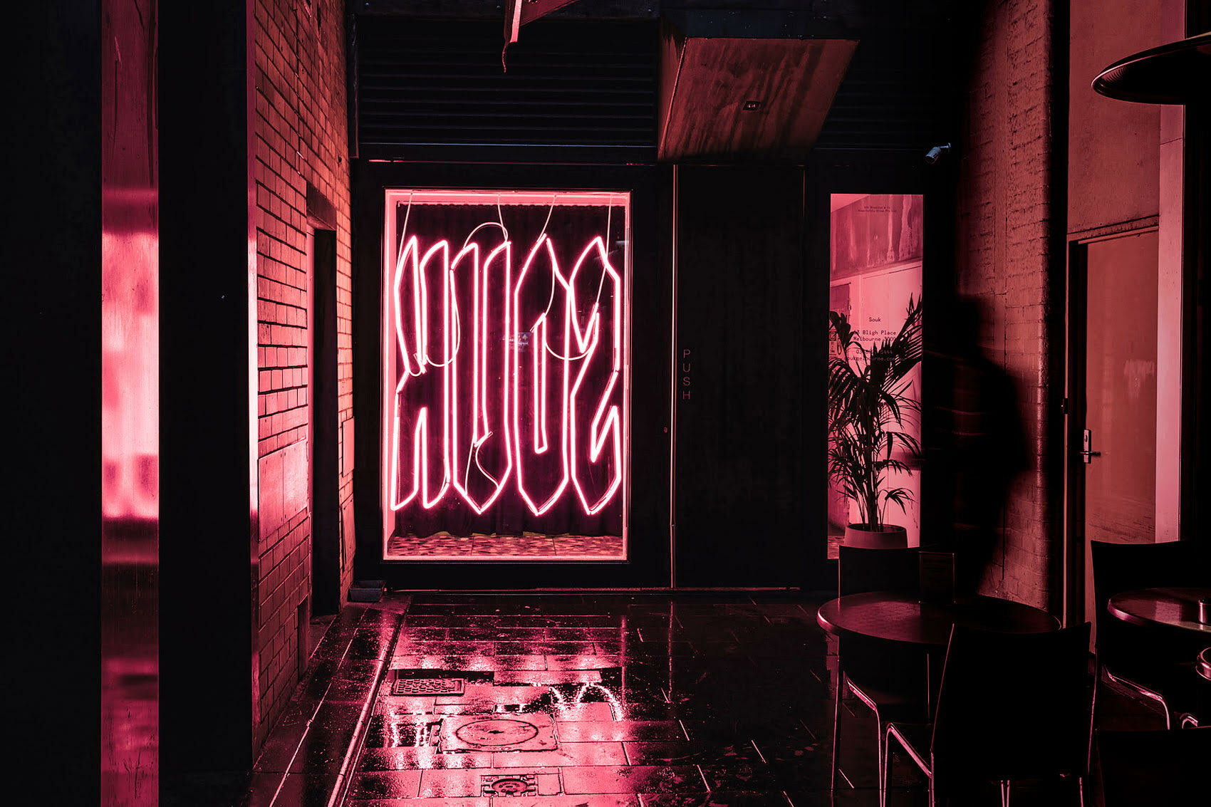 Neon pink illuminated sign reading SOUK in a shop window framed by dark brick walls and wet pavement at night