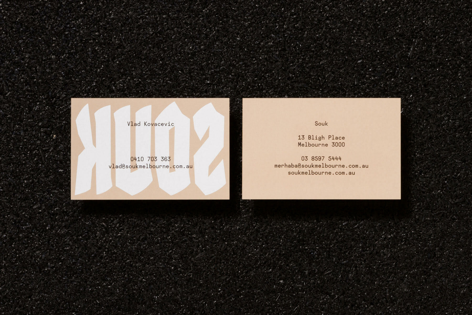 Two cream business cards for Souk featuring custom typography set against a dark textured asphalt surface