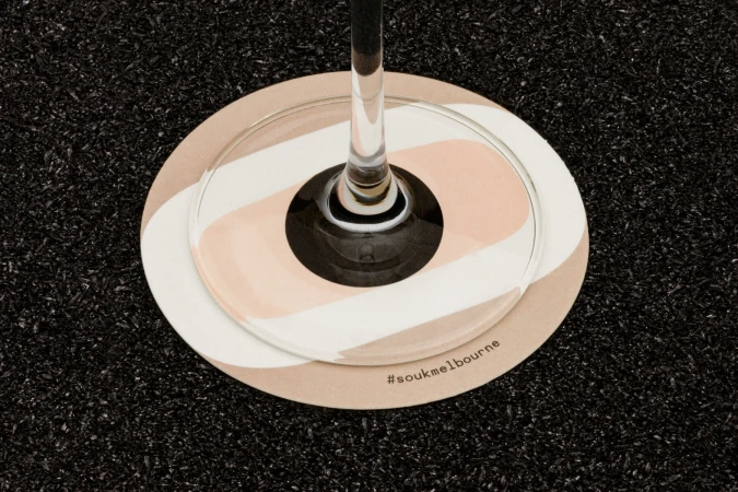 Close-up of a wine glass base resting on a round patterned coaster over a dark textured surface for Souk brand identity