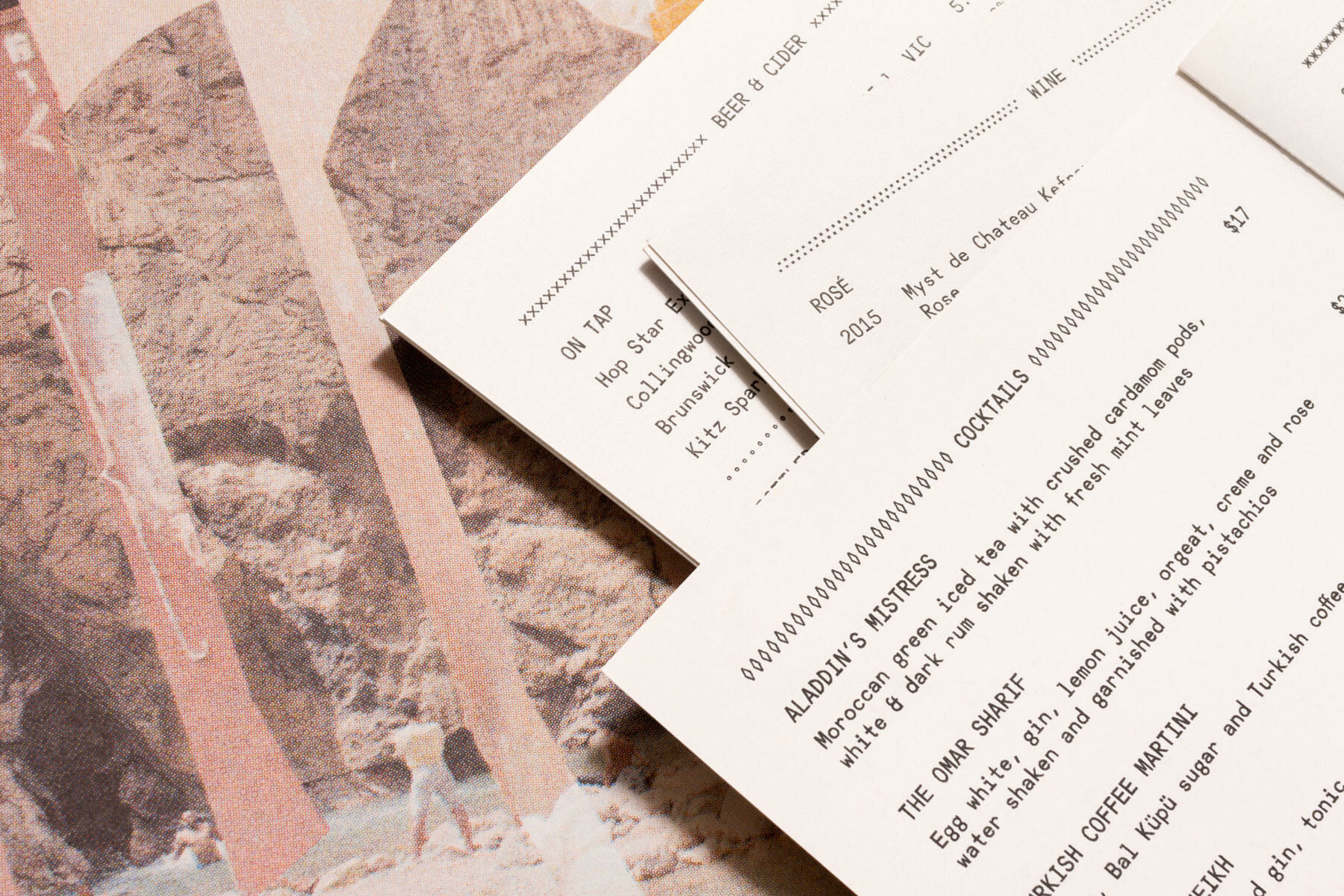 Printed beverage and cocktail menus overlapping a textured graphic page with rocky landscape imagery