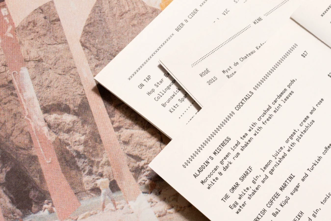 Printed beverage and cocktail menus overlapping a textured graphic page with rocky landscape imagery