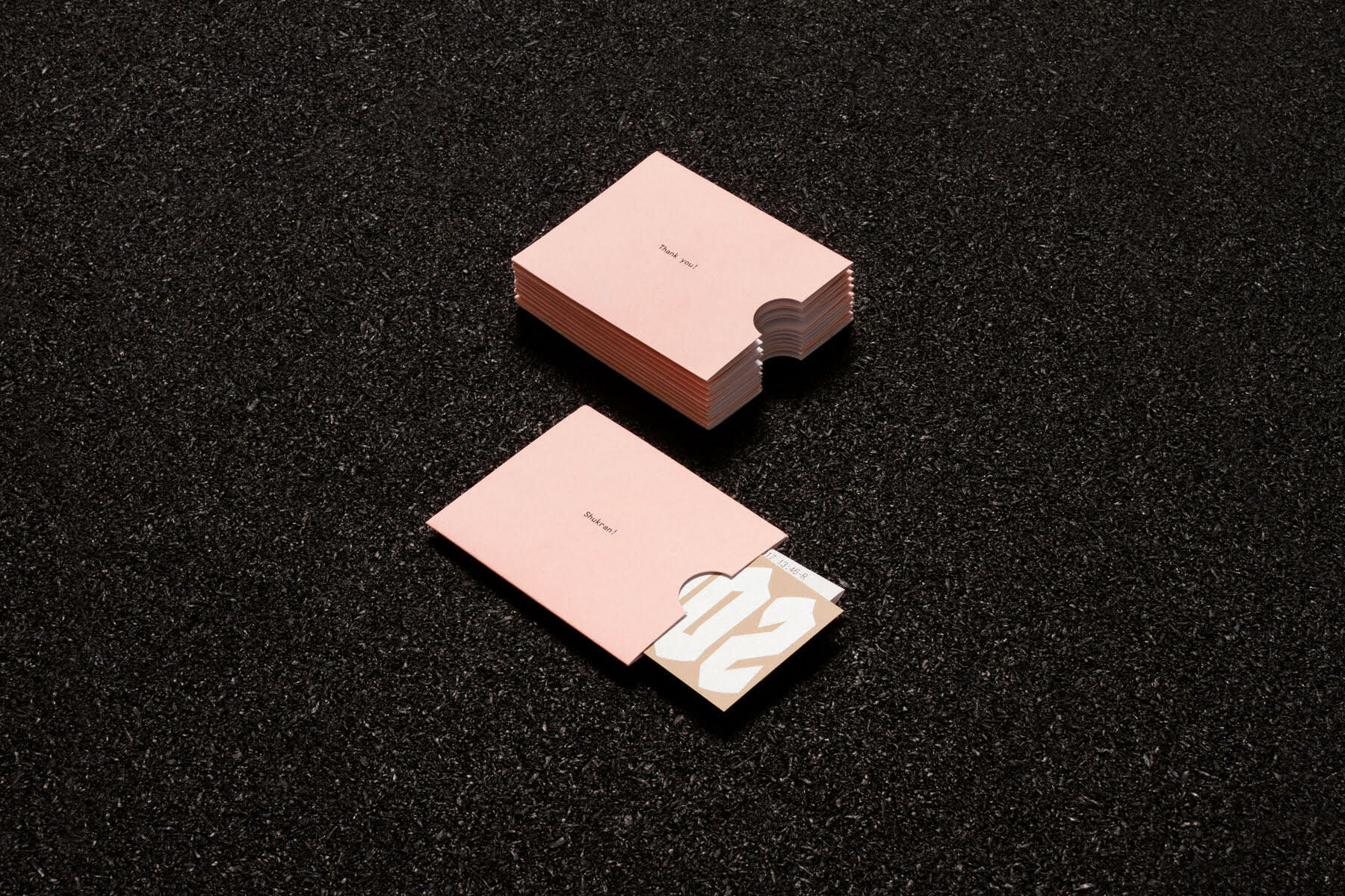 Pink paper sleeves and cards with minimalist typography resting on a dark asphalt background.