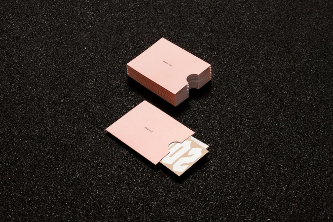 Pink paper sleeves and cards with minimalist typography resting on a dark asphalt background.