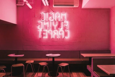 Interior cafe view featuring a glowing pink neon sign on a textured brick wall above built-in seating and small tables