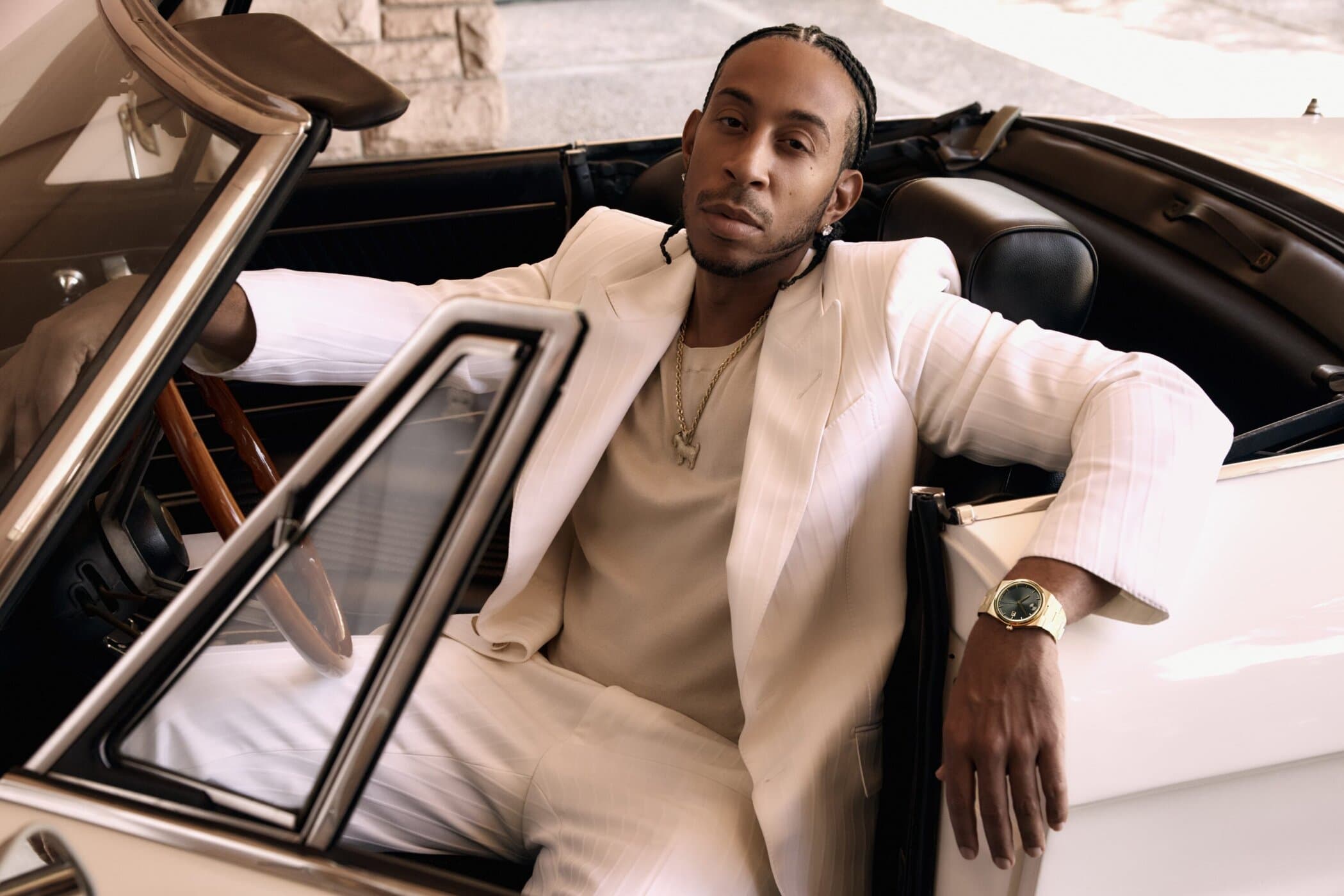Ludacris wearing a white suit seated in a vintage convertible for the Movado Fall 2025 campaign photographed by Stuart Winecoff.