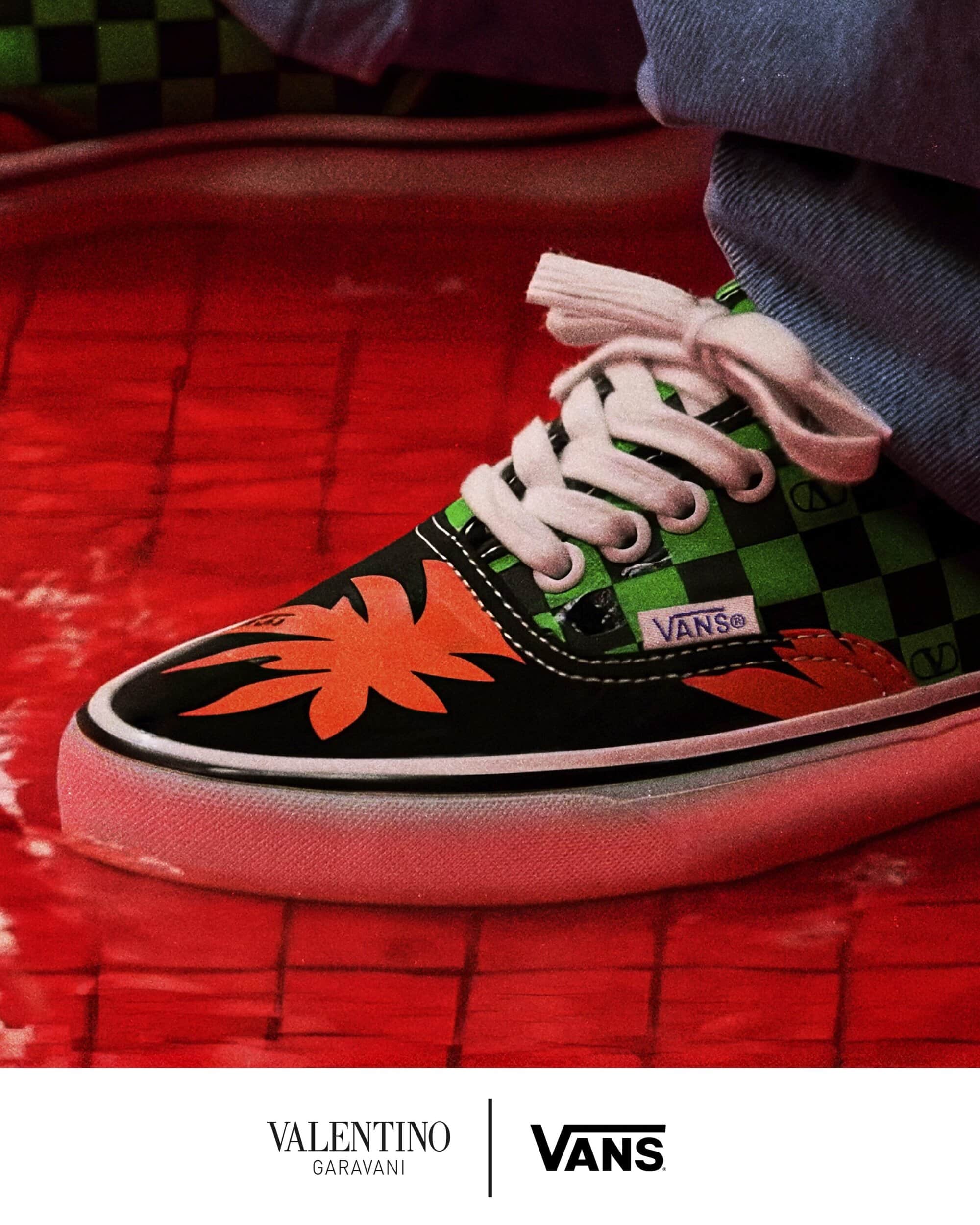 Close-up of a checkered green and black sneaker with orange flame graphics and white laces paired with denim jeans.