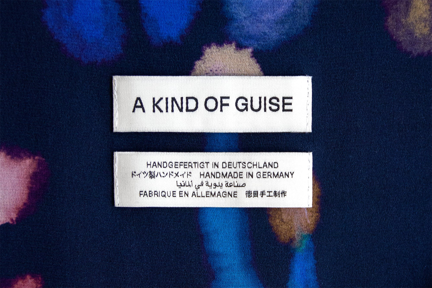 Two white clothing labels featuring black text sewn onto a dark blue patterned fabric background