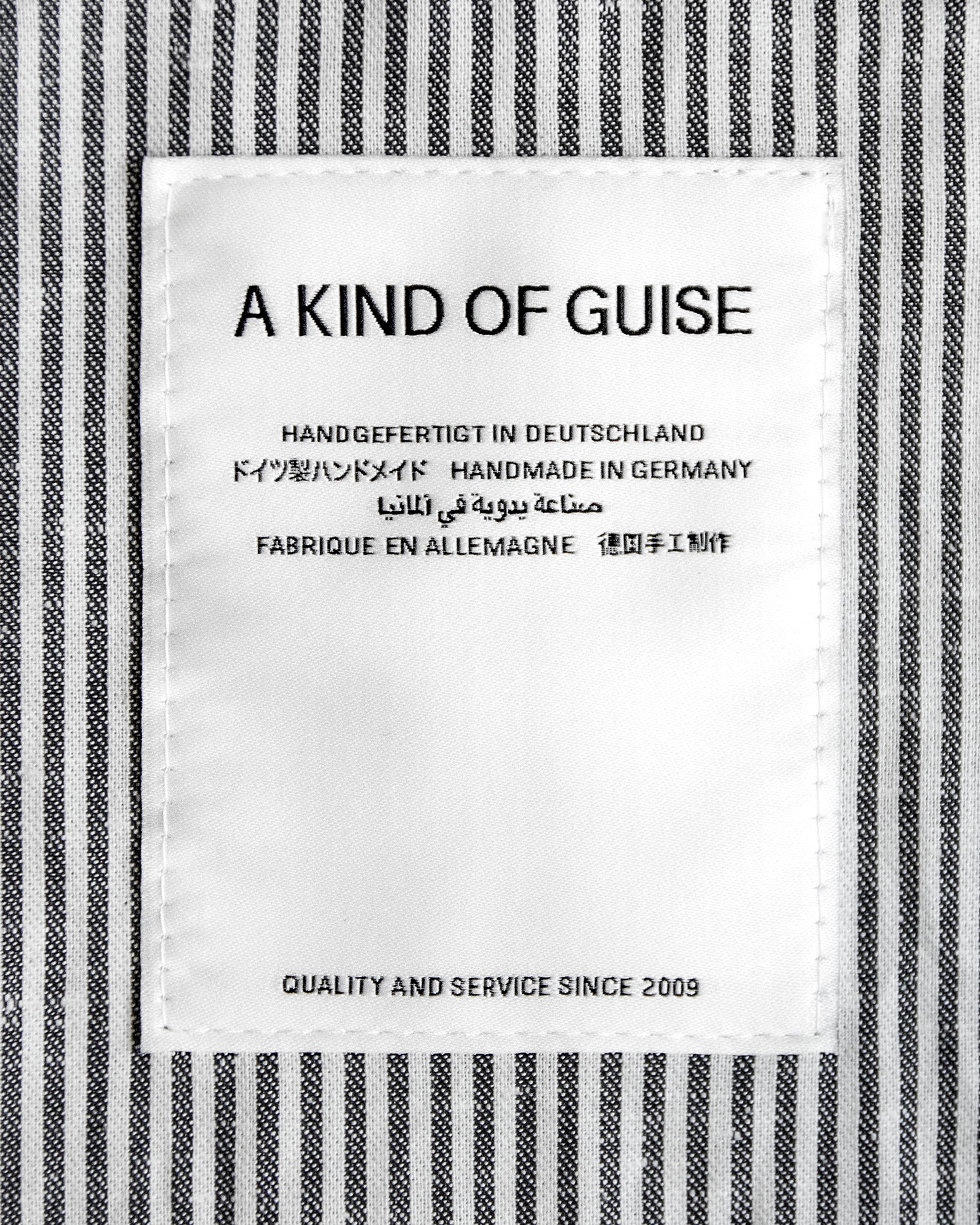 A Kind of Guise brand clothing label sewn into a black and white striped fabric background