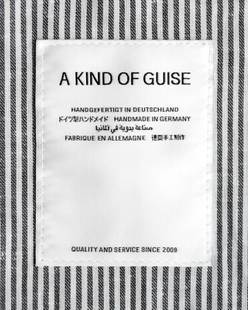 A Kind of Guise brand clothing label sewn into a black and white striped fabric background