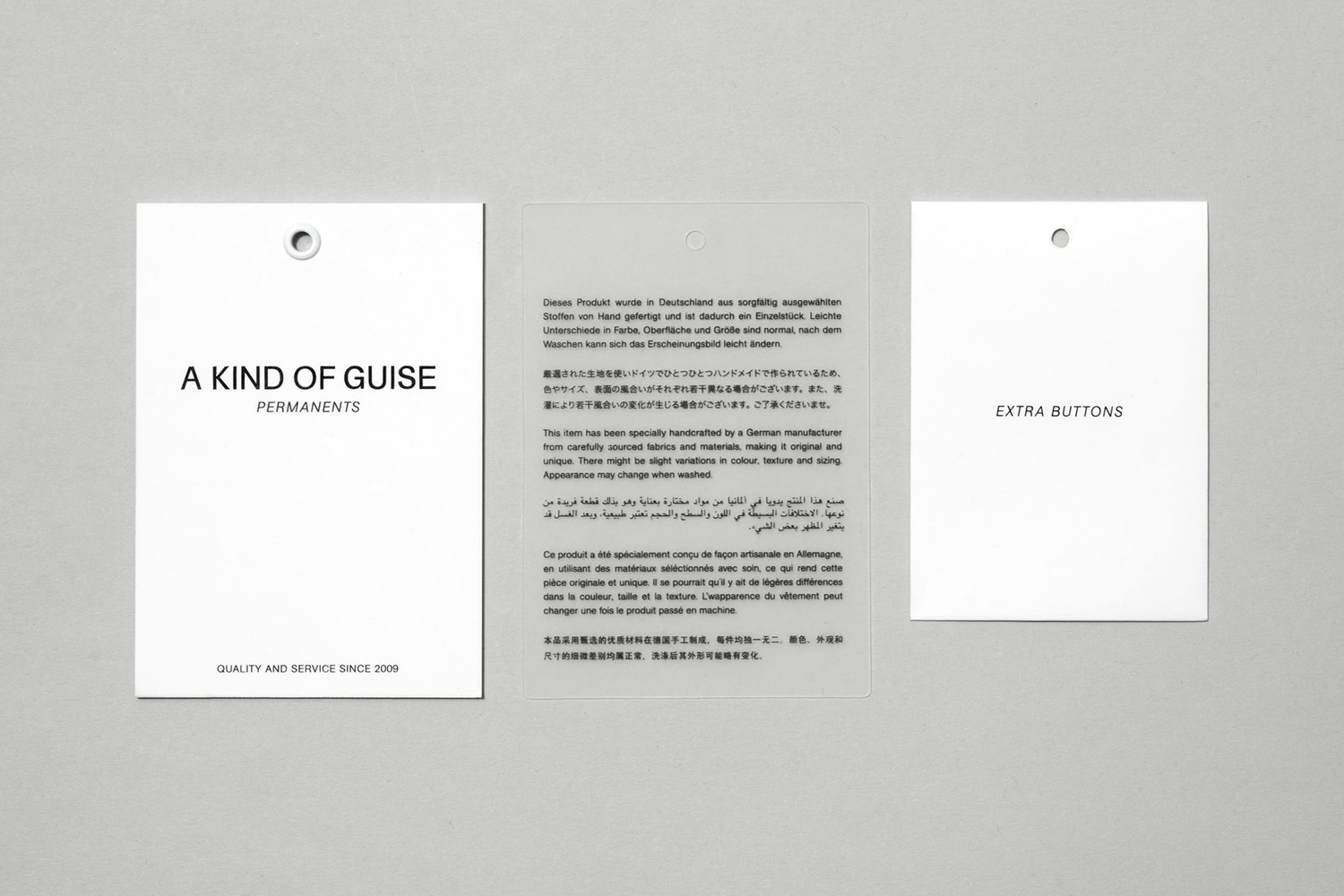 Three paper tags and labels for A Kind of Guise arrayed on a neutral grey background surface.