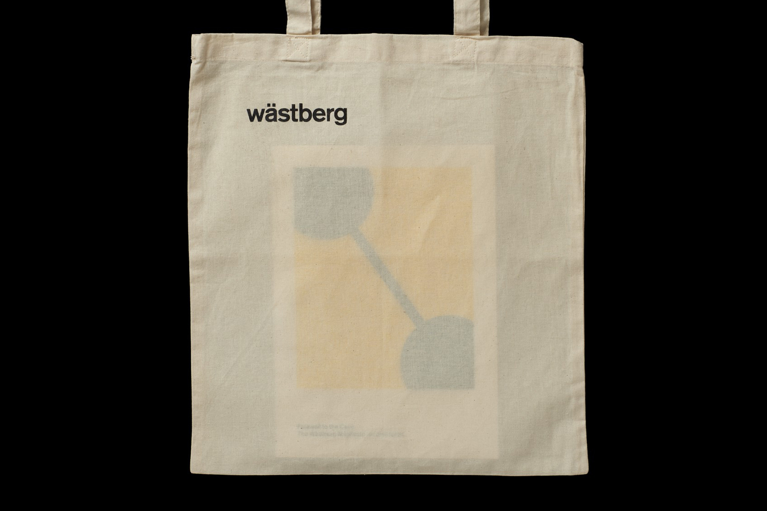 Off-white canvas tote bag with black wastbeg logo and yellow abstract graphic against dark background