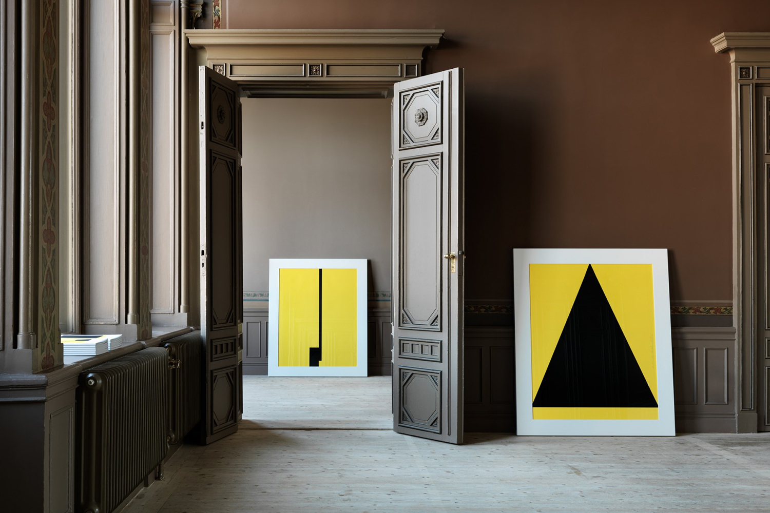 Interior shot featuring double wooden panelled doors open to reveal framed yellow and black geometric art pieces.