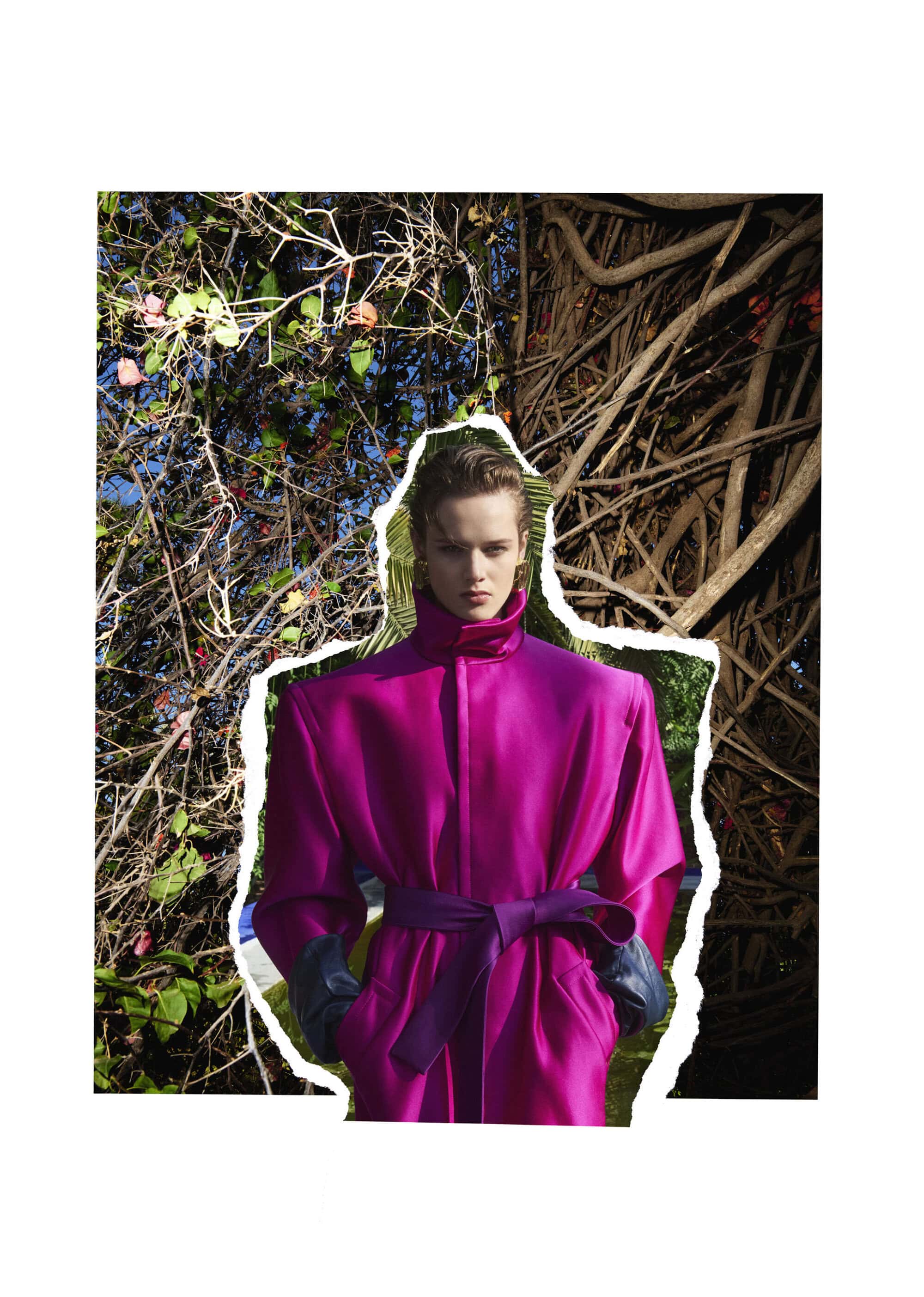 Model wearing a structured magenta coat with a purple belt against a natural foliage background in a winter editorial photograph