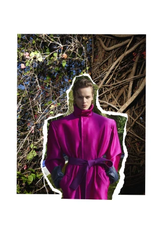 Model wearing a structured magenta coat with a purple belt against a natural foliage background in a winter editorial photograph