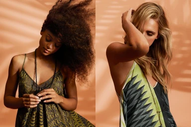 Two fashion models wearing patterned dresses and long necklaces against a warm peach backdrop with leaf shadow patterns.