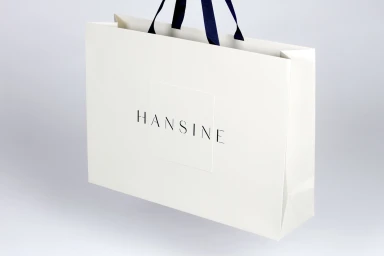 White paper shopping bag with navy ribbon handles and Hansine logo on a clean white background