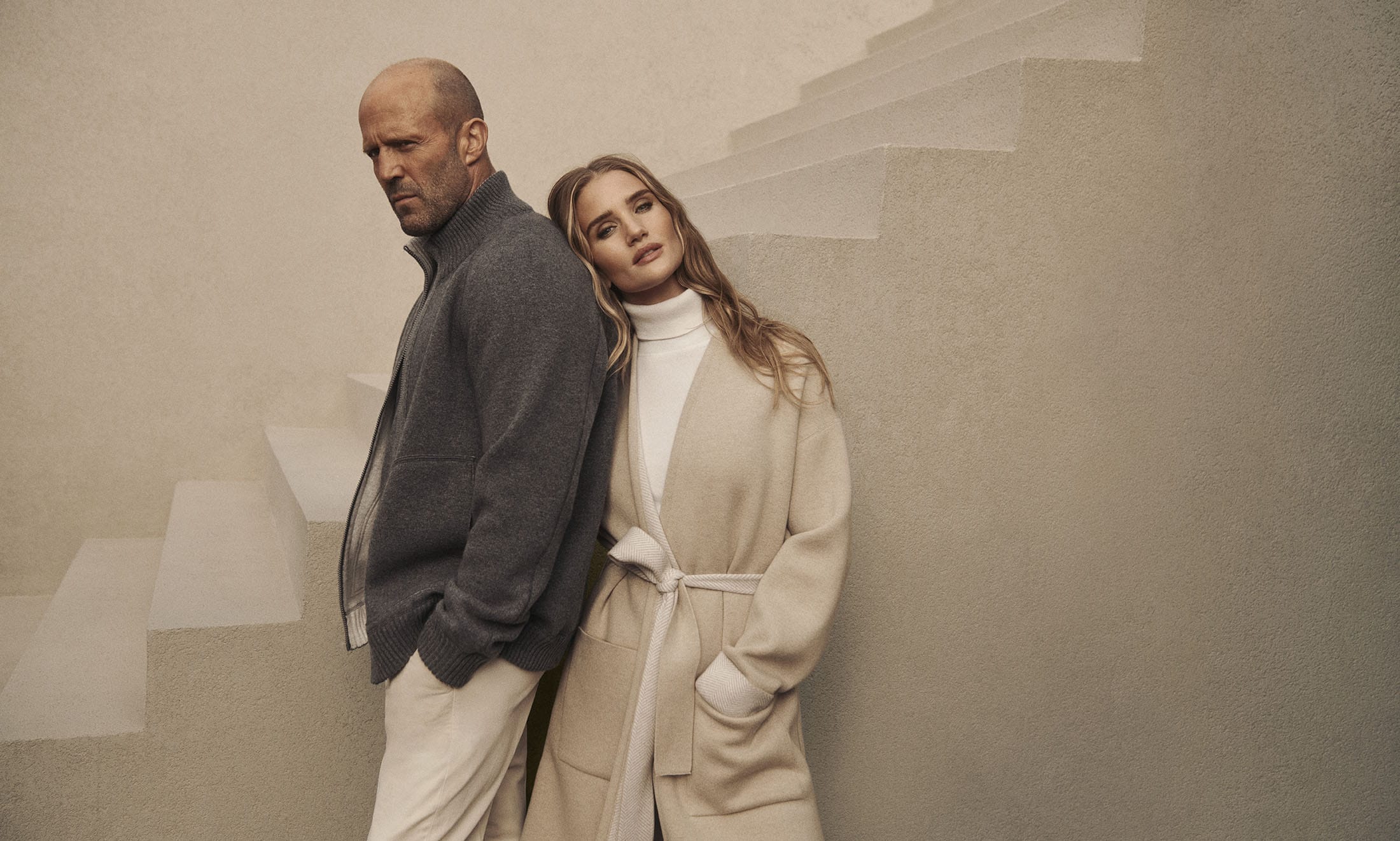 Jason Statham and Rosie Huntington-Whiteley posing against a neutral textured staircase for Falconeri