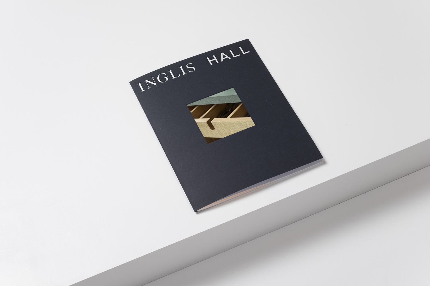 Dark booklet with Inglis Hall branding and a square cutout resting on a minimal white surface