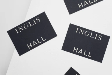 Black business cards featuring Inglis Hall branding arranged on a white textured background.