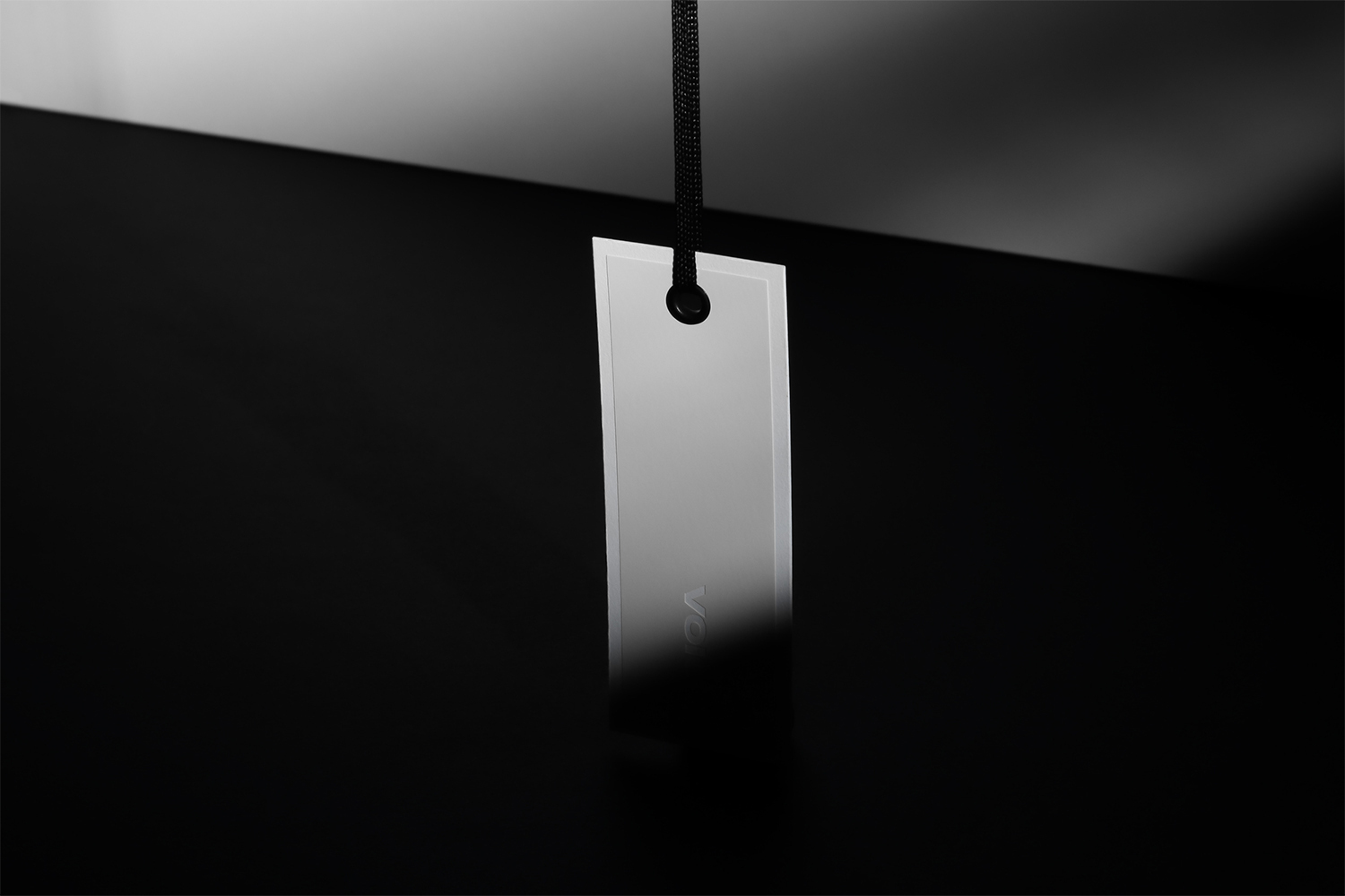Minimalist white hanging tag suspended by a black cord against a dark gradient background with sharp lighting.