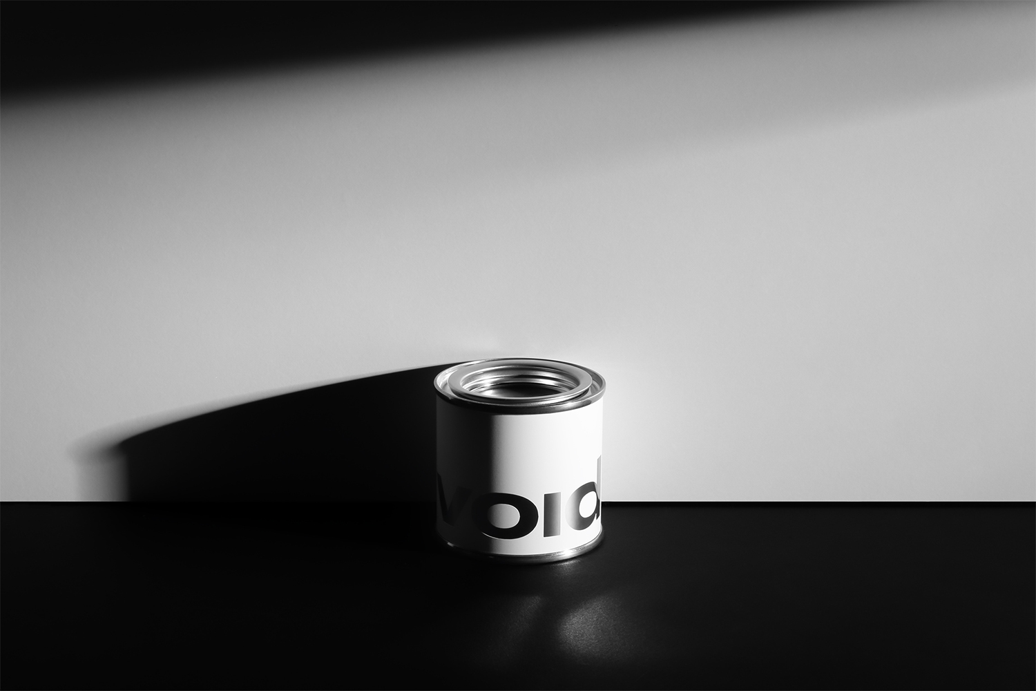 A small cylindrical container branded with the word VOID sits on a dark surface against a light grey background with stark directional shadows.