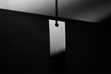 Minimalist white hanging tag suspended by a black cord against a dark gradient background with sharp lighting.