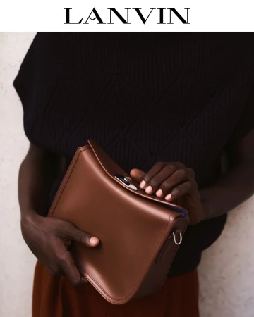 Model holding a structured brown leather handbag against a pale textured background for Lanvin Fall 2025.