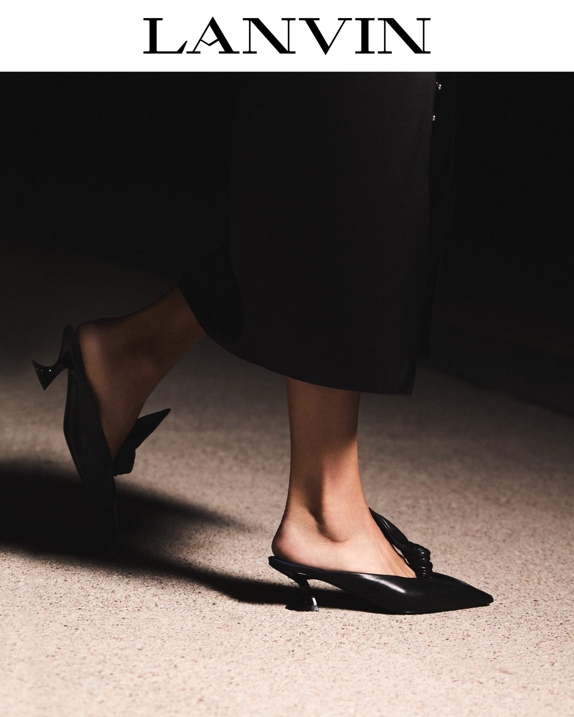 Close-up of a person walking wearing black leather pointed-toe mules and a dark skirt for a Lanvin editorial shoot.