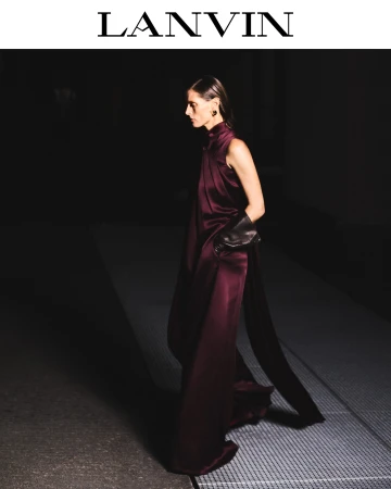Model wearing a deep burgundy silk gown and leather gloves standing on a paved surface for a Lanvin fashion editorial.