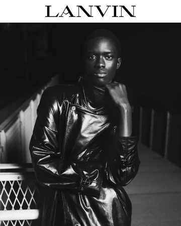 Black man wearing a dark glossy leather coat posing in a high-contrast black and white editorial fashion portrait for Lanvin.