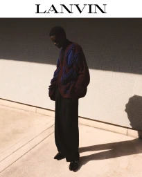 Model standing outdoors wearing a dark textured patterned cardigan and black trousers against a tiled wall