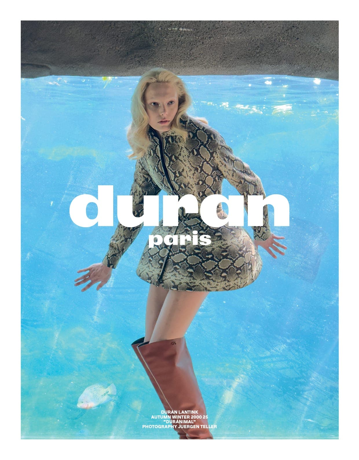 Model wearing snakeskin jacket and brown boots standing in bright blue water for Duran Lantink campaign
