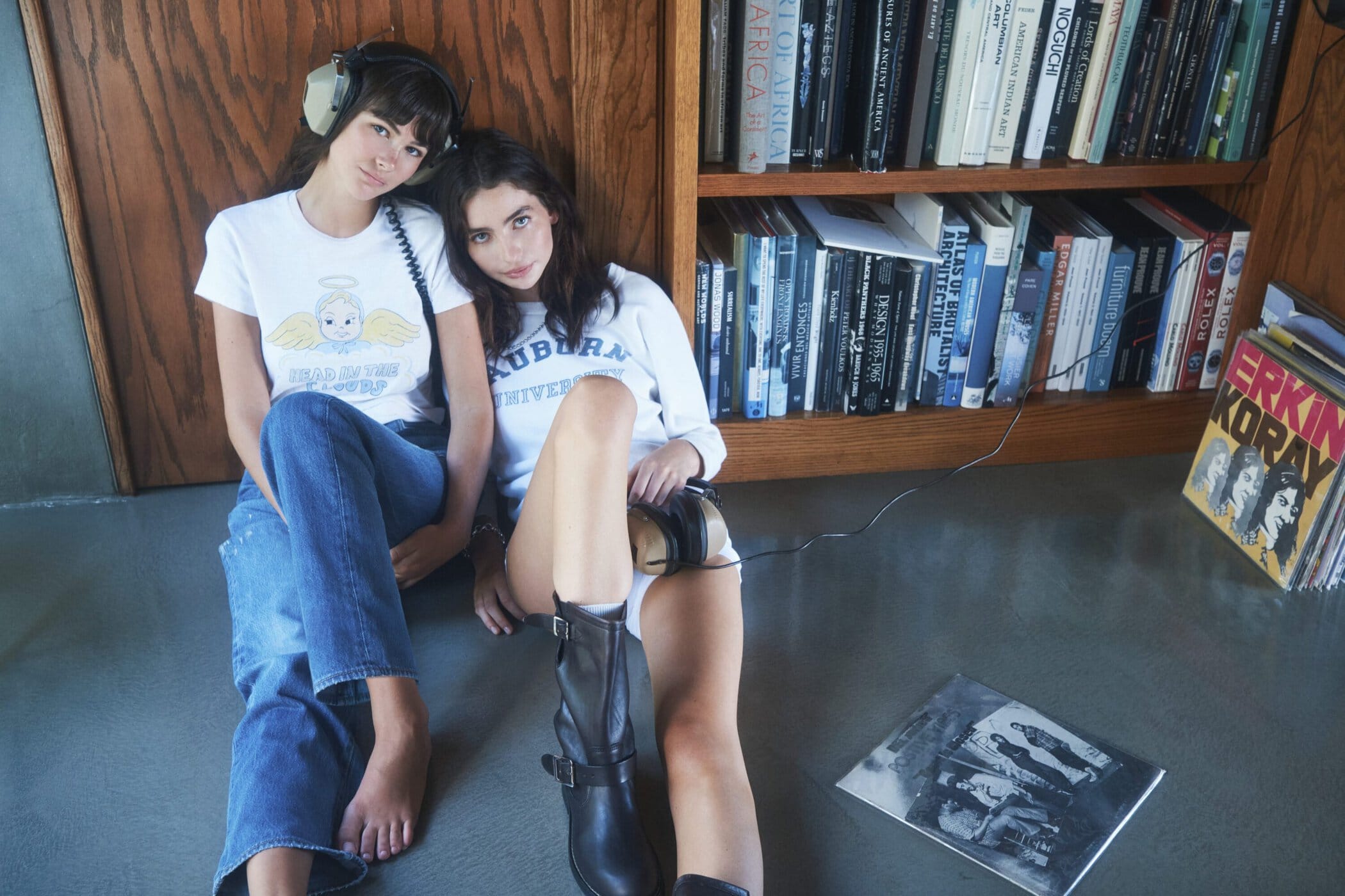 Two female models sitting against a wooden bookcase wearing graphic t-shirts and jeans for RE/DONE Fall 2025 campaign.