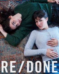 Two women lying on an ornate patterned rug wearing knit sweaters and denim jeans for RE/DONE