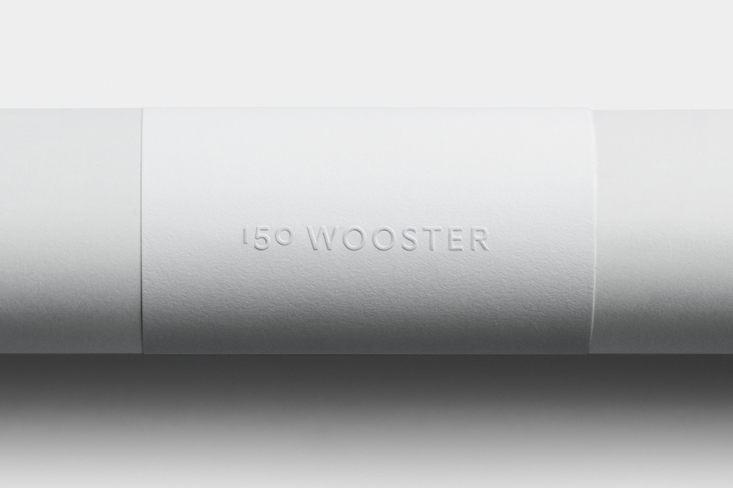 Embossed paper band wrapping around a white cylinder featuring 150 Wooster brand identity design by Javas Lehn Studio.