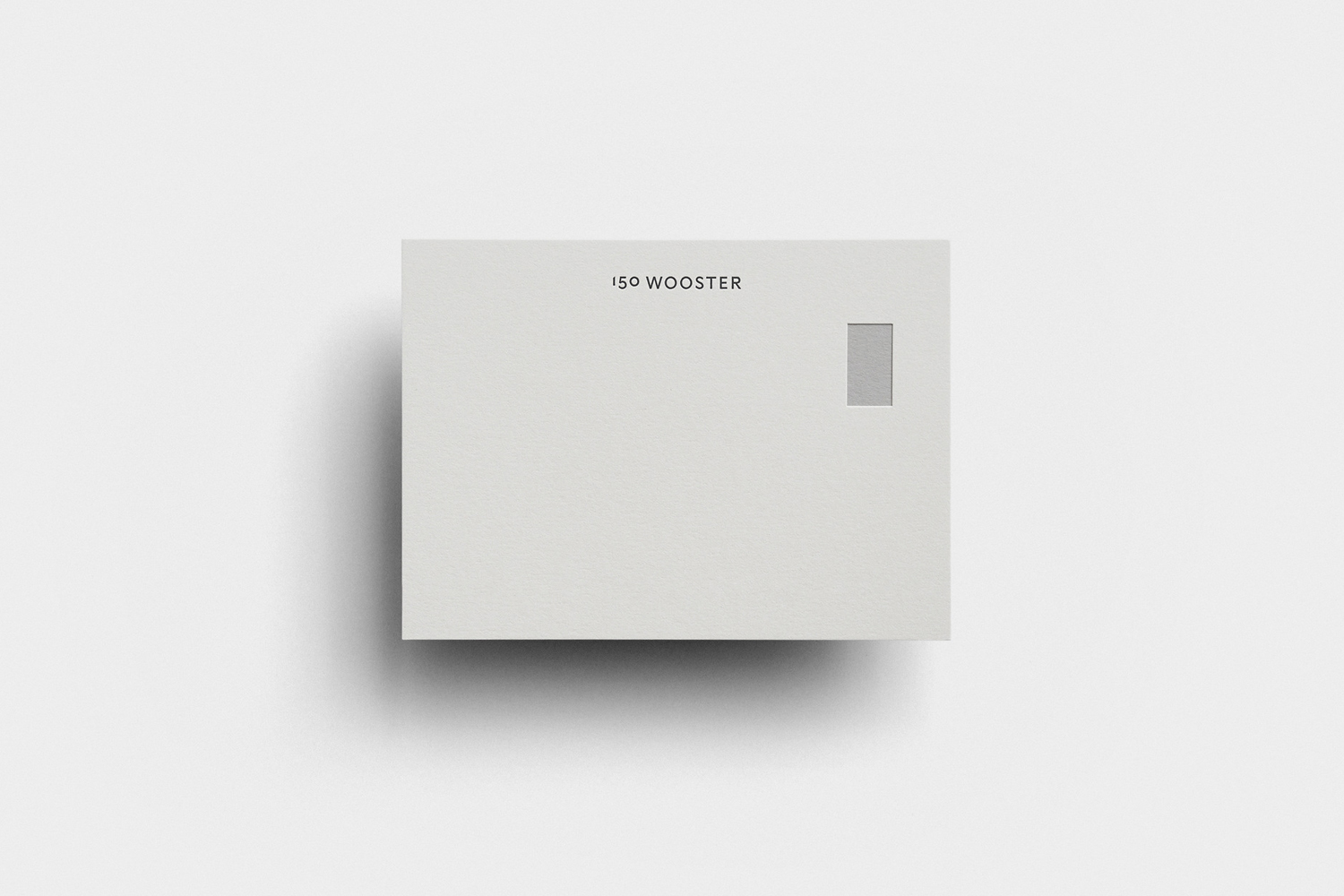 Minimalist stationery card with debossed text 150 Wooster and a small window against a light grey background