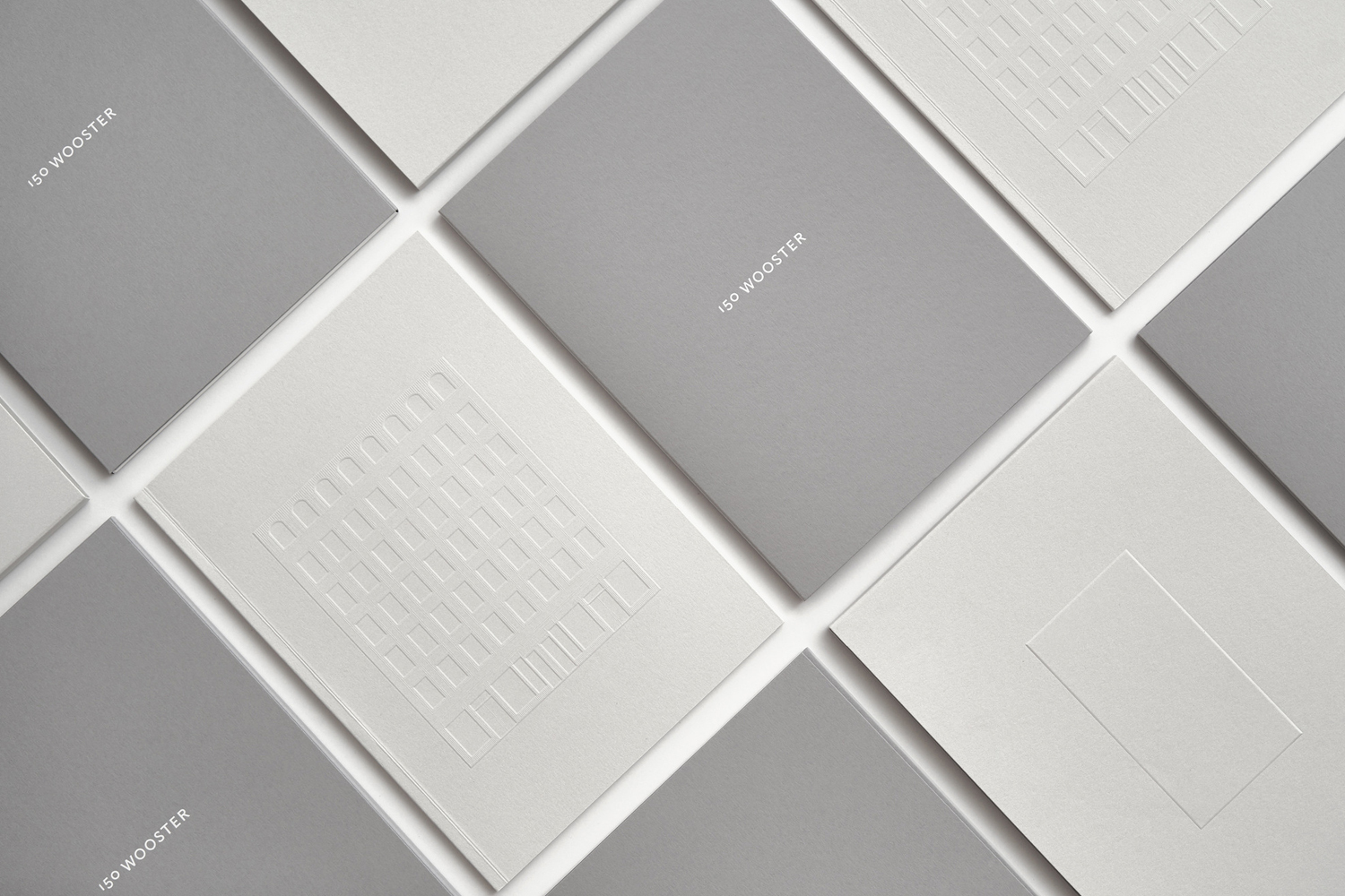 An arrangement of grey and white minimal booklets with embossed architectural details and 150 Wooster typography.