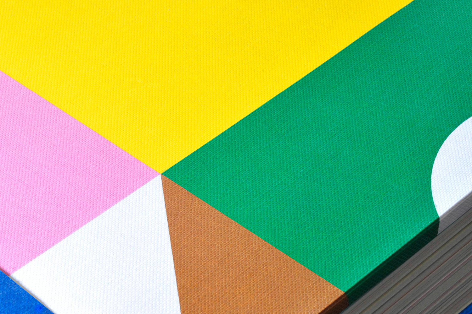 Close-up macro shot of a book cover with bold geometric colour blocking in yellow, green, pink, brown, and white.