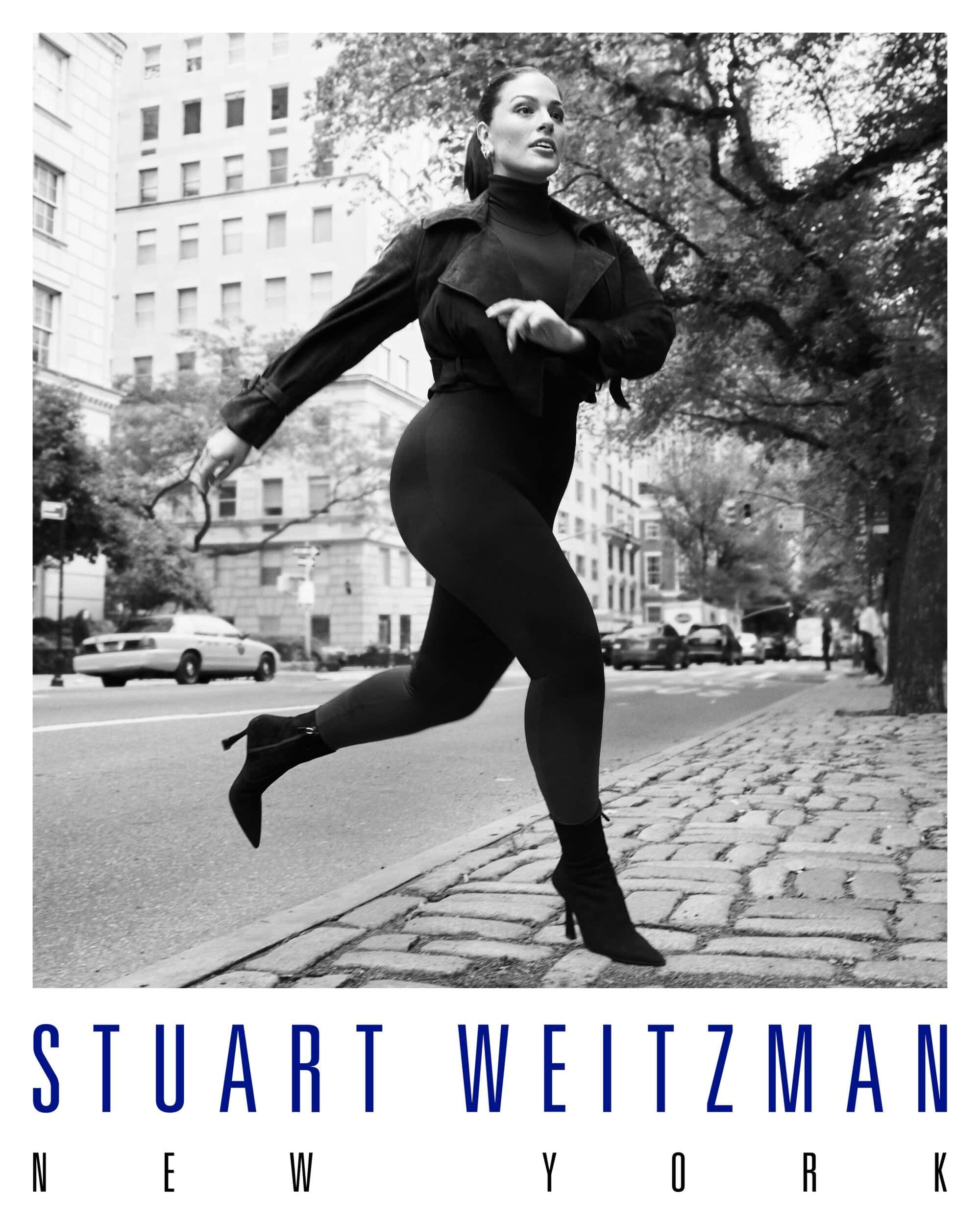Ashley Graham walking on a New York sidewalk wearing a dark jacket and heeled boots for Stuart Weitzman campaign