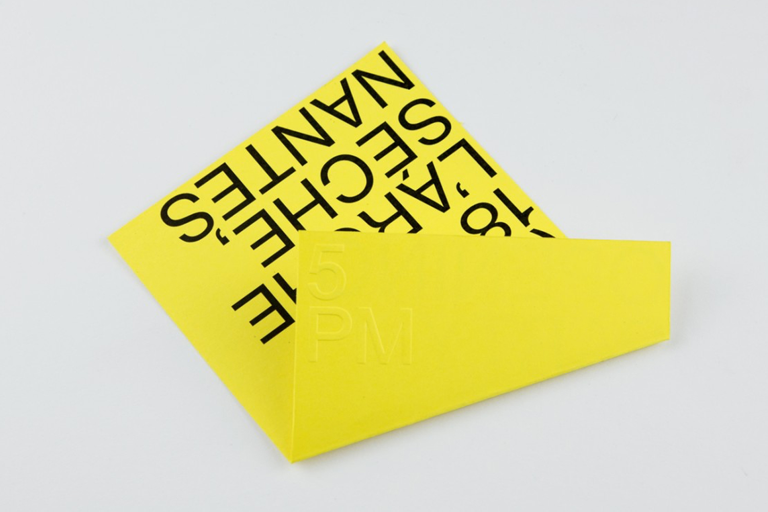 Folded yellow paper card with bold black typography and embossed branding on a plain white background