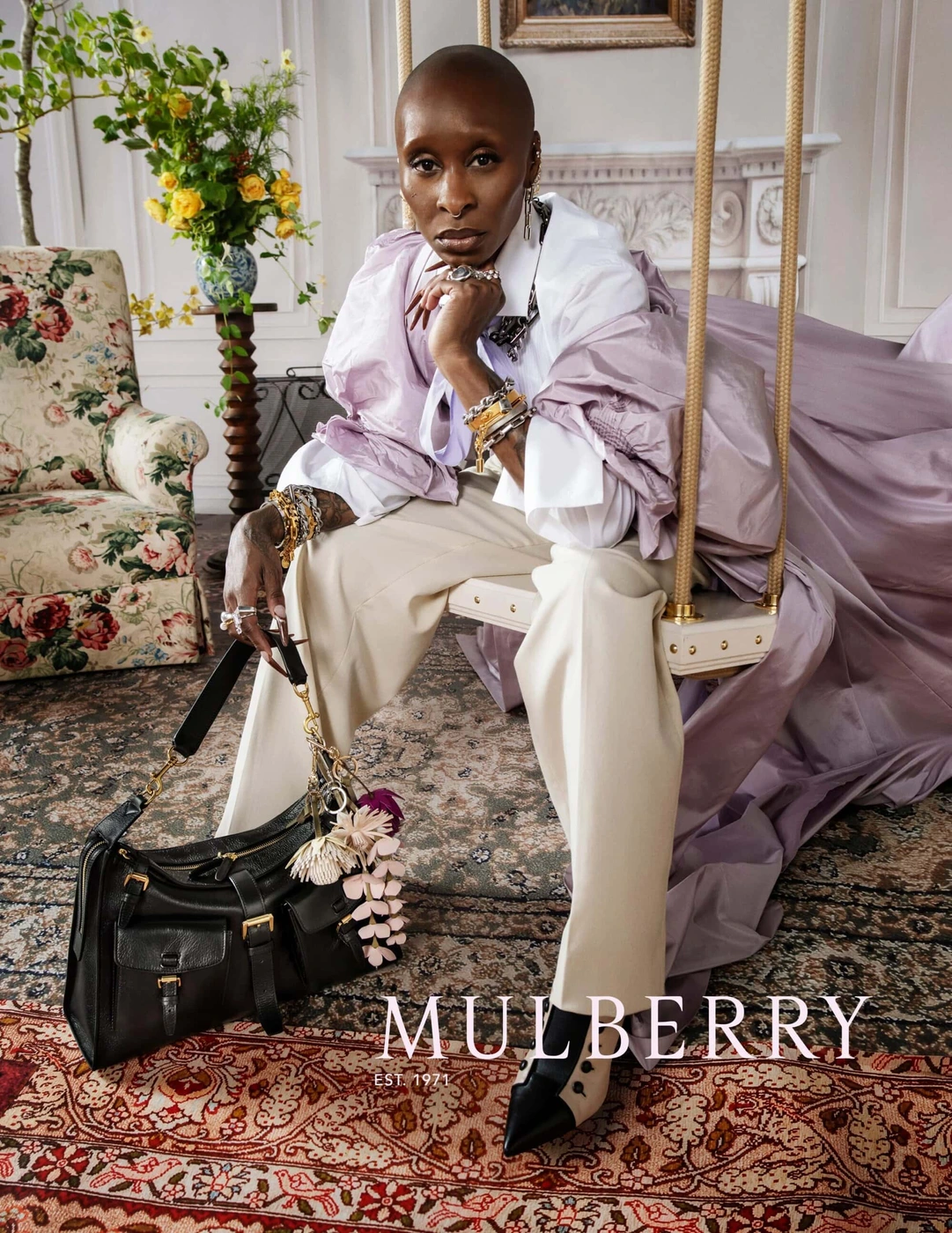 Cynthia Erivo seated on an indoor swing holding a black leather handbag for Mulberry Spring 2026 ad campaign.