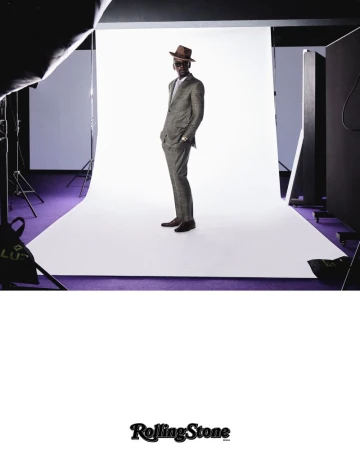Full-length shot of a stylish adult man in a checkered suit and hat, standing in a photo studio with white backdrop and purple floor.