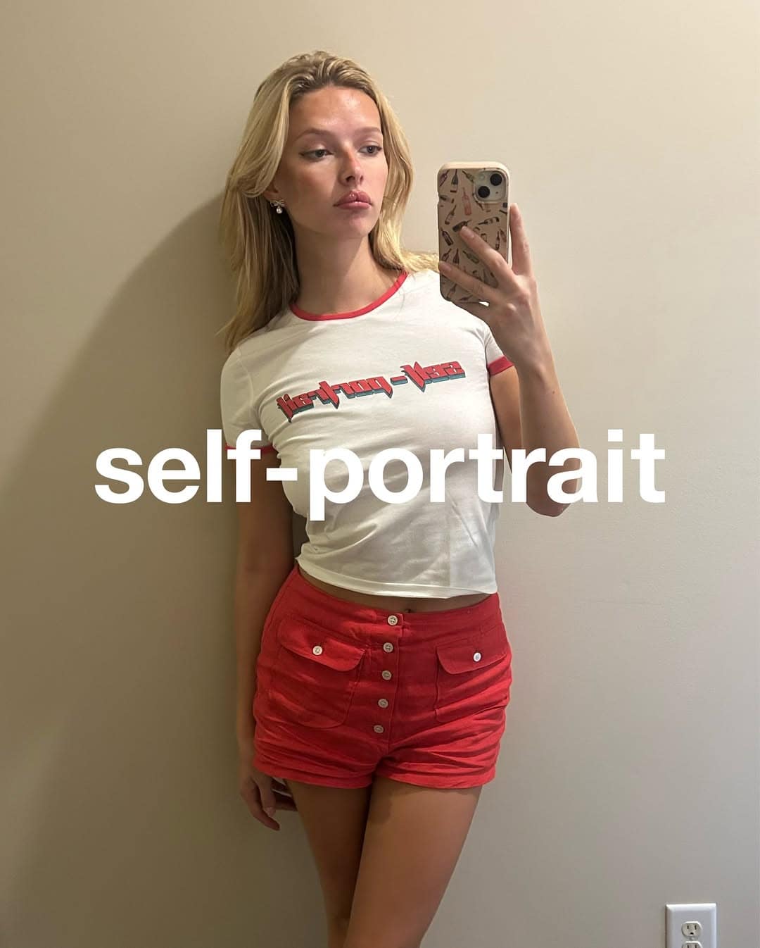 Apple Martin taking a mirror selfie wearing a white ringer t-shirt and red shorts for Self-Portrait Fall 2025.