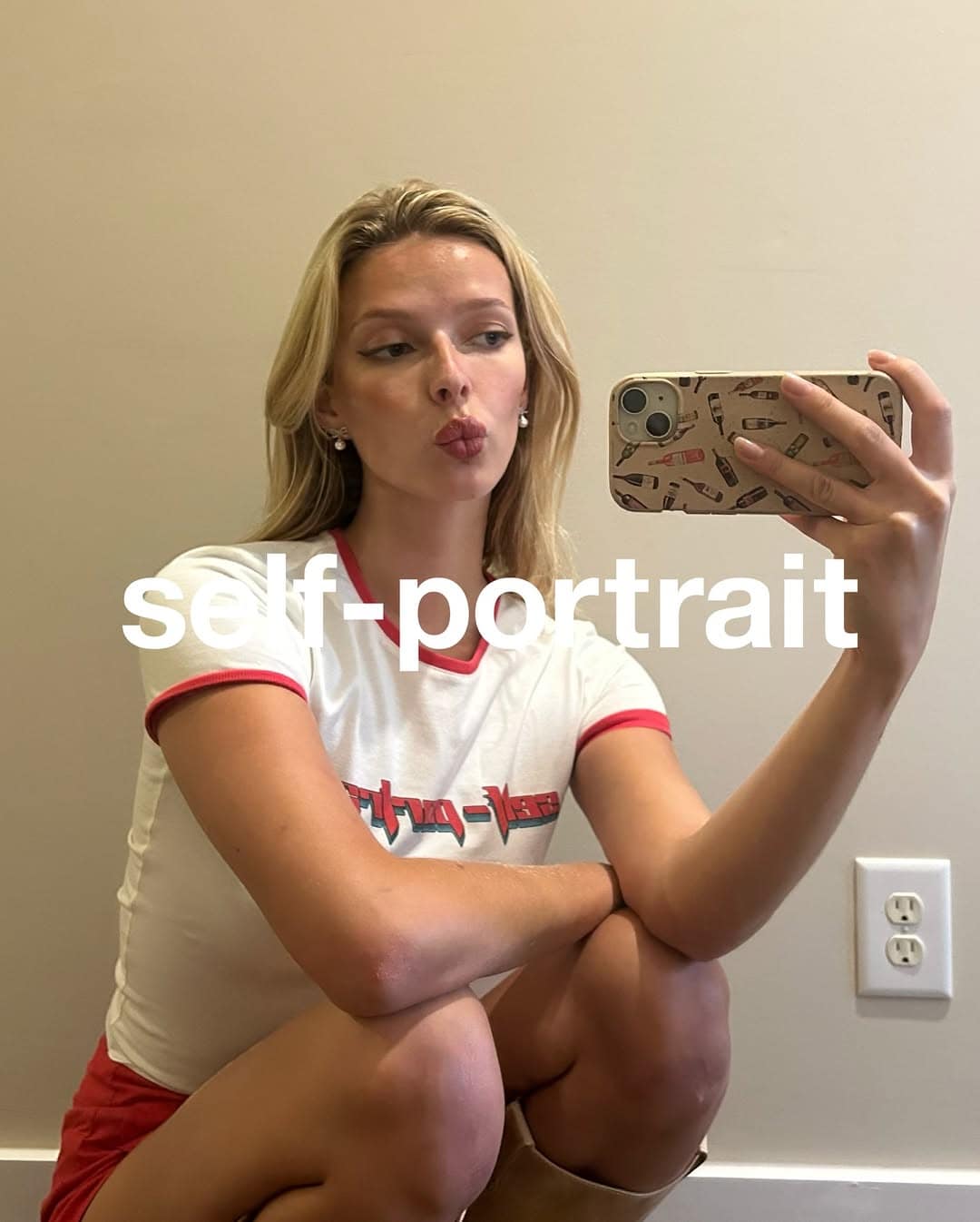 Model Apple Martin taking a mirror selfie for Self Portrait wearing a white ringer t shirt with red trim