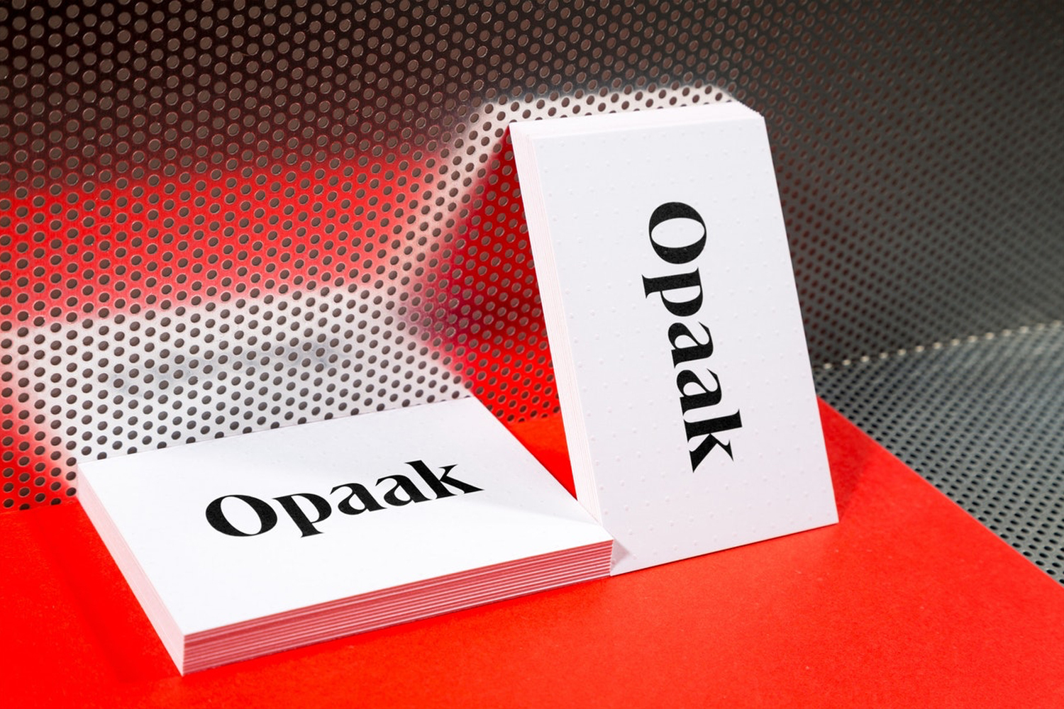 Stacked business cards featuring the brand name Opaak in black serif typography on white paper set against a red and perforated background.